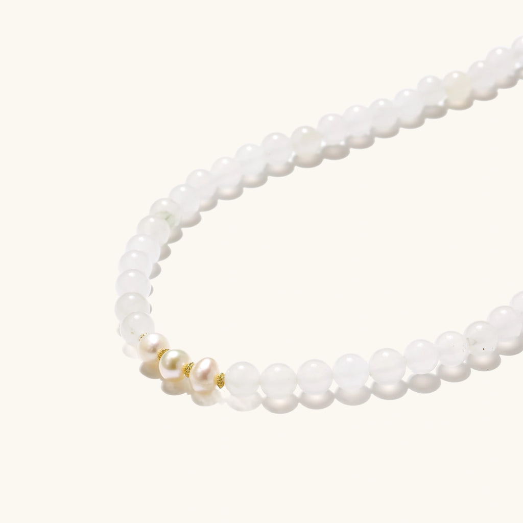 Three layered white beaded bracelets with carved orange agate lotus centerpiece and freshwater pearls on cream background.