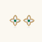 Gold quatrefoil stud earrings with white mother-of-pearl petals and emerald green gemstone center on beige background.