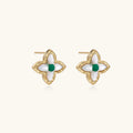 Gold quatrefoil stud earrings with white mother-of-pearl petals and emerald green gemstone center on beige background.