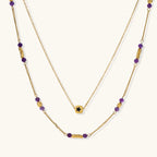 Two layered gold-tone necklaces with purple stone beads and star pendant against cream background.