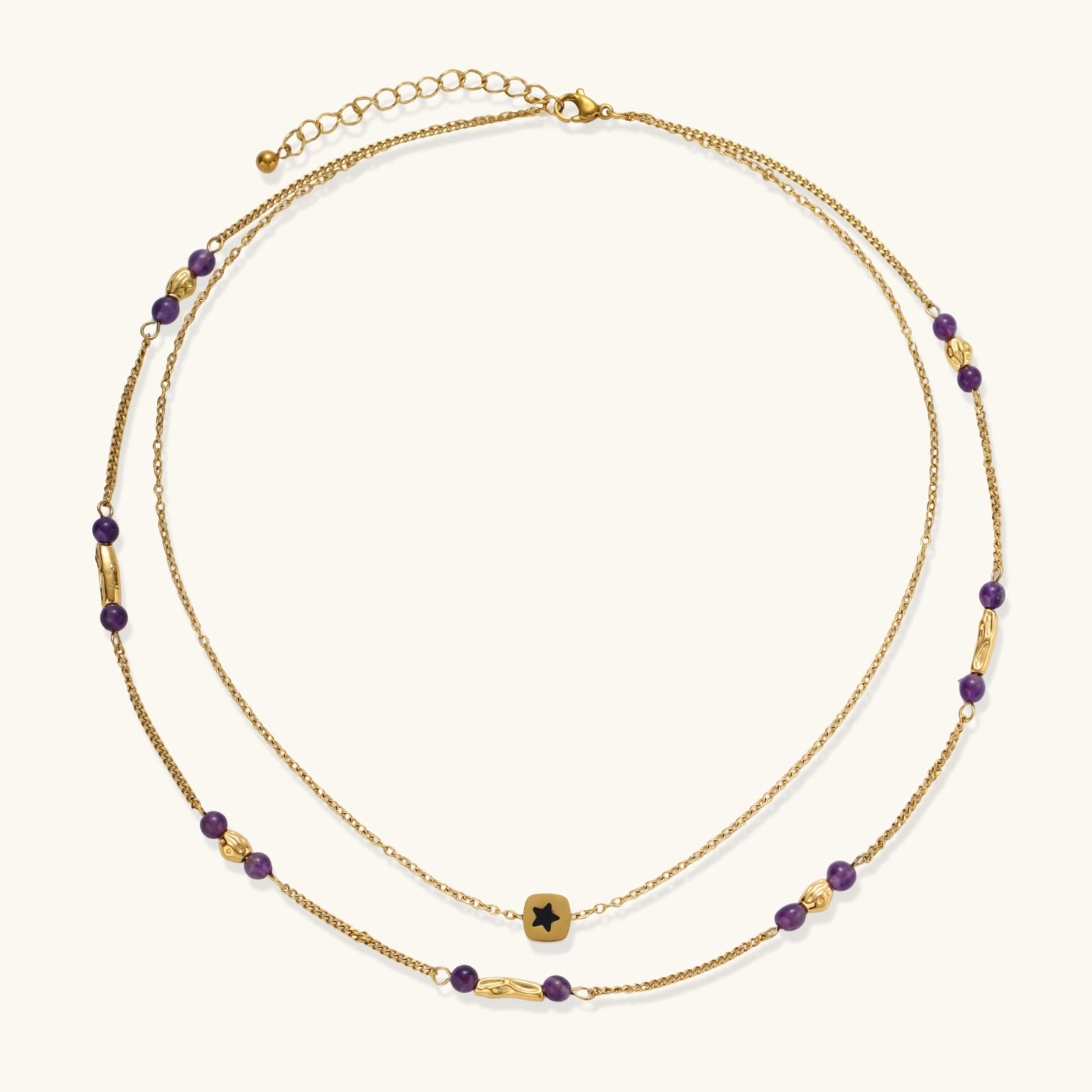 Two layered gold-tone necklaces with purple stone beads and star pendant against cream background.
