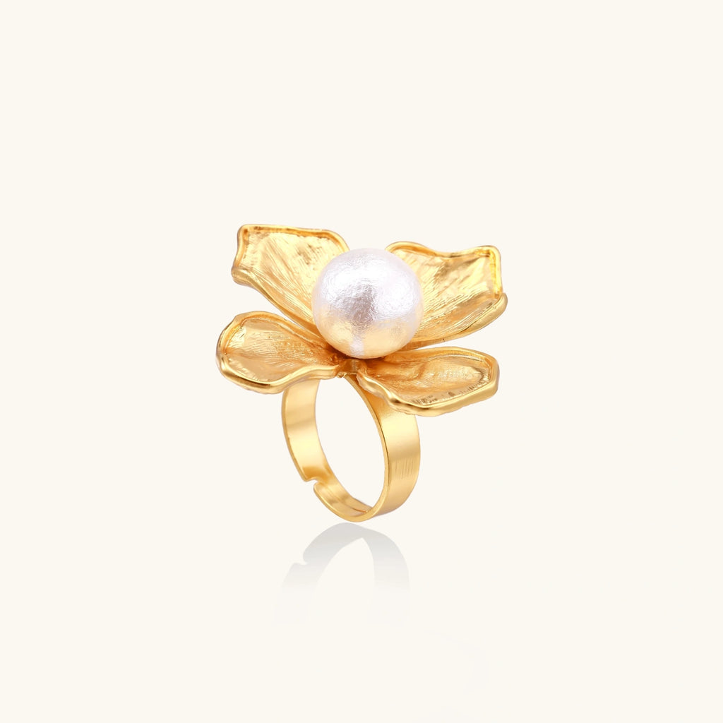 Gold-plated flower ring with textured petals and white cotton pearl center on cream background